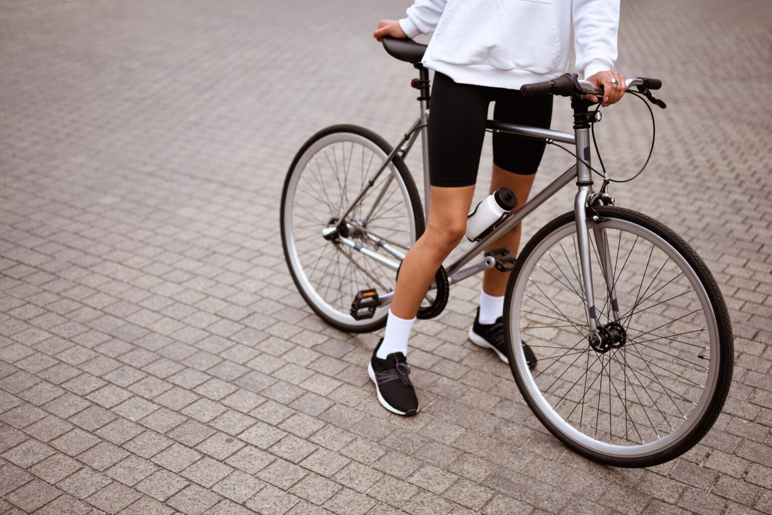 Faceless shot of african american woman in hoodie and cycling shorts standing near bicycle on street